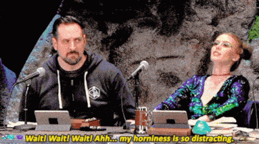a man and a woman are sitting at a table with microphones and the woman is saying wait ! wait ! wait !