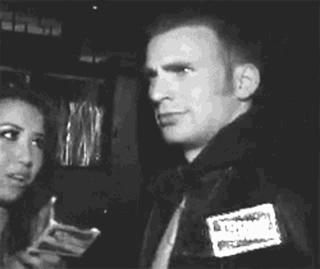 a black and white photo of a man holding a microphone and talking to someone .