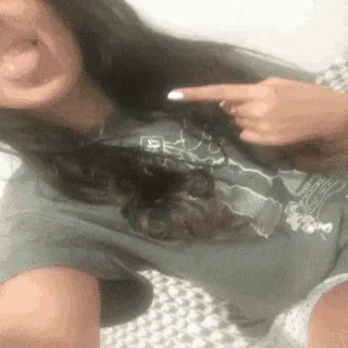 a woman is taking a selfie with her tongue out and pointing at her chest .