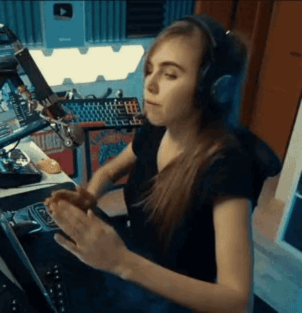 a woman wearing headphones is eating a donut while sitting at a desk in front of a computer .