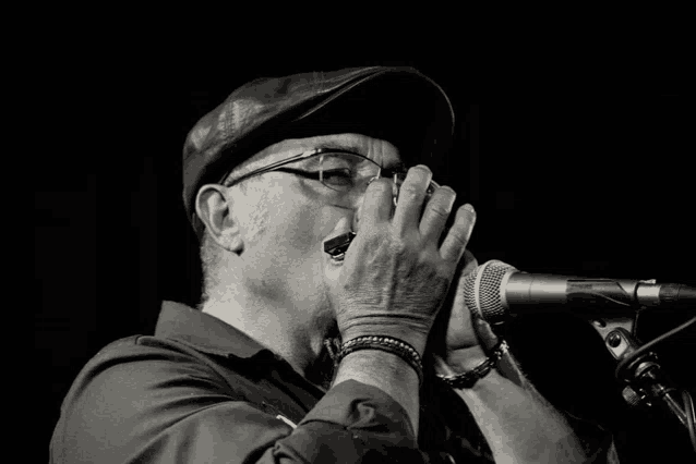 a man wearing glasses and a hat playing a harmonica in front of a microphone