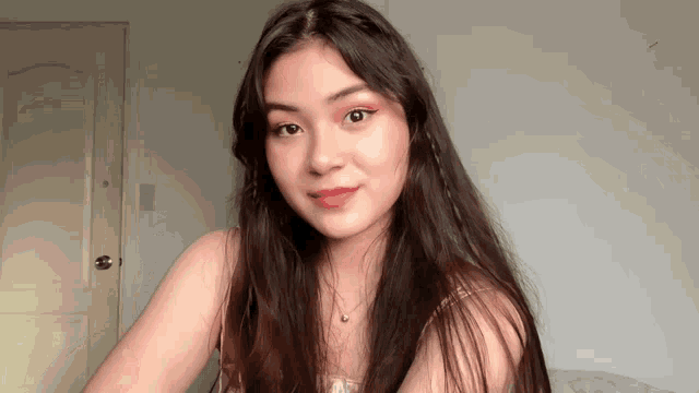 a woman with long dark hair wearing a pink top and a necklace