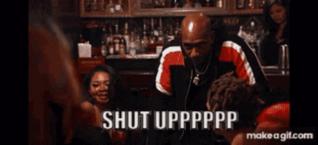 a man in a red and black jacket is standing in front of a group of people and says shut upppppp