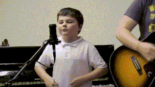 a boy is singing into a microphone while a man plays a guitar
