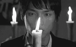 a black and white photo of a man holding a lit candle in front of his face .