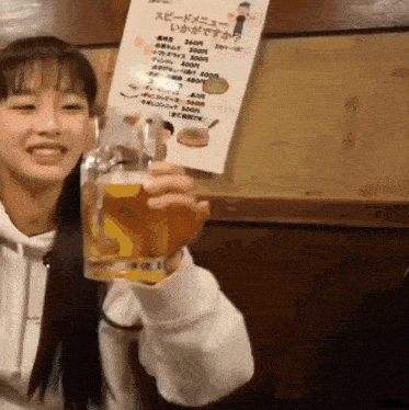 a woman is holding a glass of beer in front of a menu in another language
