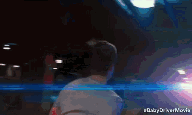 a man in a white shirt is standing in a dark room with a baby driver movie written on the bottom of the screen