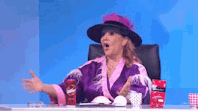 a woman in a purple robe and black hat is sitting at a table with a can of pringles on it .