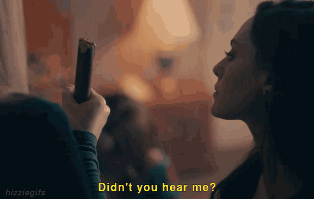 a woman in a dark room is holding a cell phone and says did n't you hear me