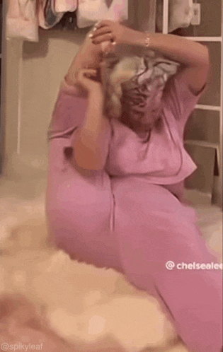 a woman in a pink shirt is sitting on a bed with her hair in a braid