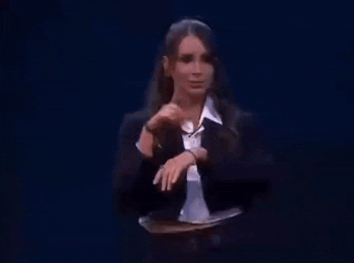 a woman in a suit and white shirt is standing on a stage and giving a speech .