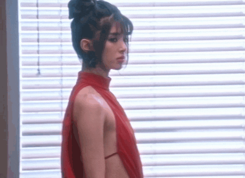 a woman is standing in front of a window wearing a red dress .