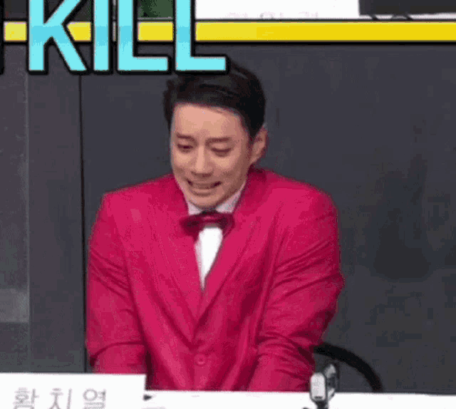 a man in a red suit and bow tie is sitting at a desk with smoke coming out of his face .