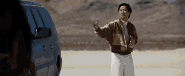 a man is standing in front of a car in the desert and giving the middle finger .