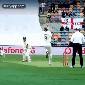 a cricket game is being played on a field with a chelsea flag in the background