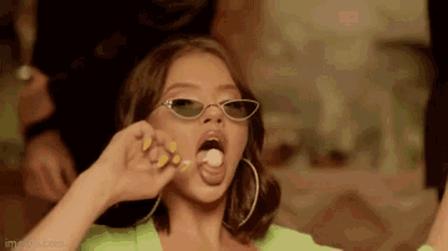 a woman wearing sunglasses and hoop earrings is eating a lollipop .