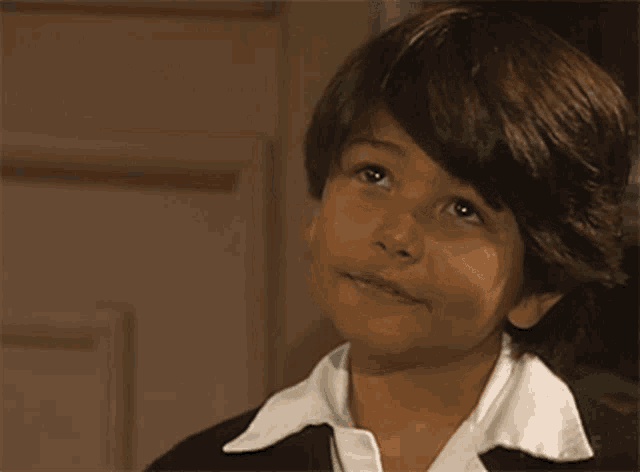 a young boy wearing a black jacket and white shirt is smiling