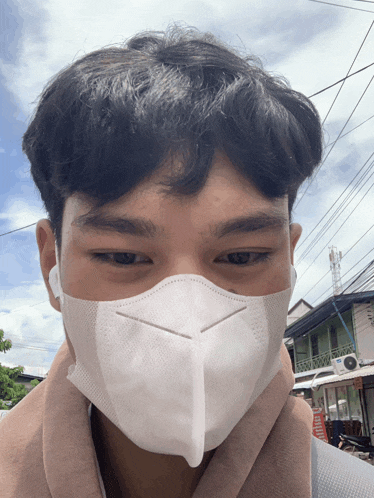 a young man wearing a white face mask looks at the camera with a building in the background