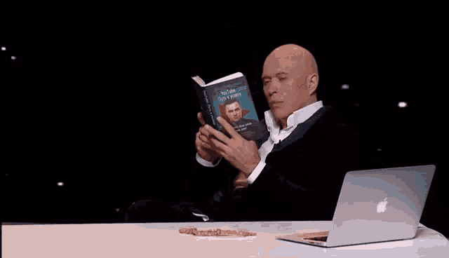 a man is sitting at a table with a laptop and throwing a trash can .