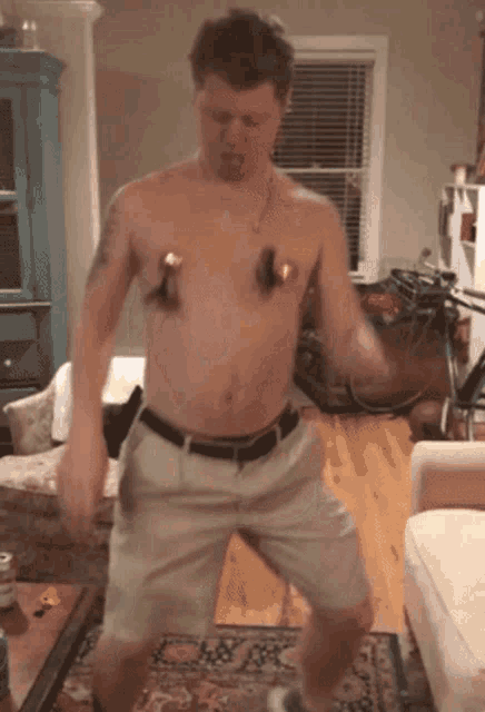 a shirtless man is dancing in a living room with a couch in the background