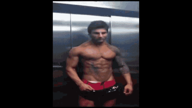 a muscular man in red shorts is flexing his arms in a gym