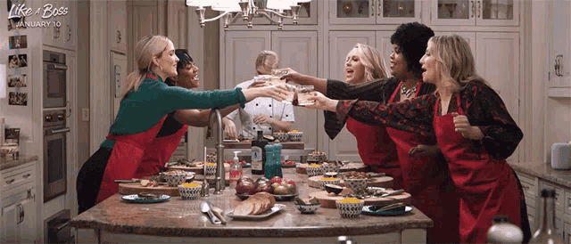 a group of women wearing red aprons are toasting in a kitchen