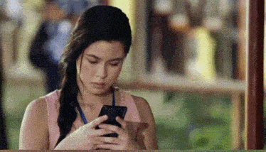a woman in a pink shirt is looking at her cell phone