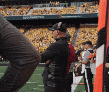 a man stands in front of a sign that says " go hawkeyes "