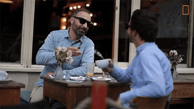 two men are sitting at a table with a sign that says ' a ' on it