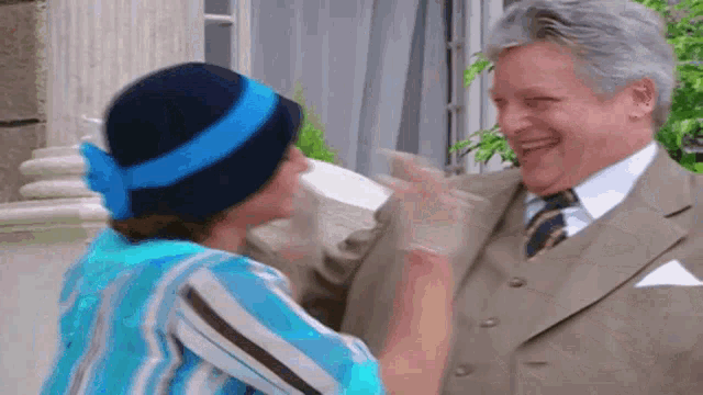 a man in a suit and tie is hugging a woman in a hat .