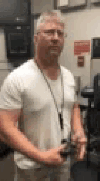 a man in a white shirt and glasses is standing in a room with his arms crossed .