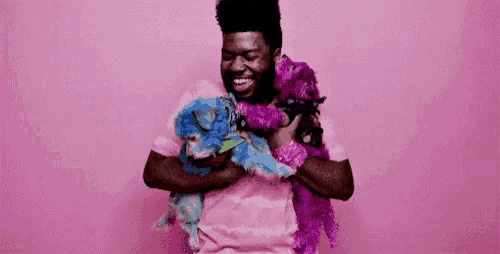 a man in a pink shirt is holding a bunch of stuffed animals .