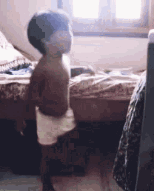 a baby is standing in front of a bed in a room .