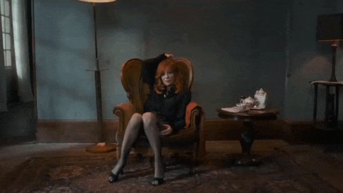 a woman with red hair sits in a chair with her legs crossed