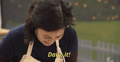 a woman in an apron is saying dang it while looking down .