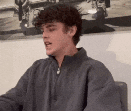 a young man with curly hair is sitting in a chair in front of a painting of an airplane .