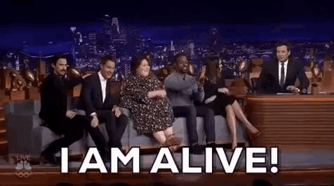 a group of people sitting on a couch with the words i am alive written on the screen