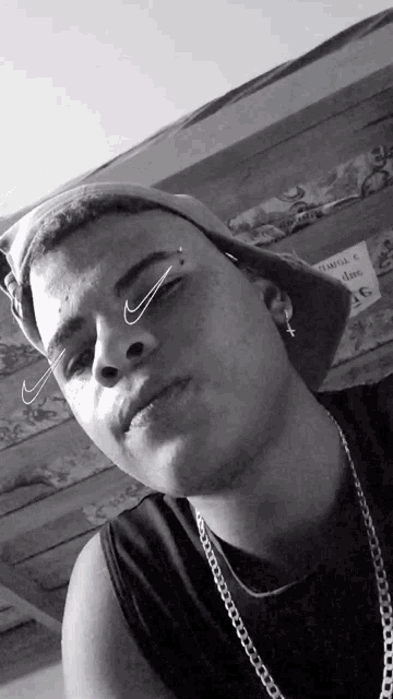 a black and white photo of a young man wearing a hat and chains