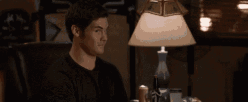 a man is sitting at a table with a lamp in the background
