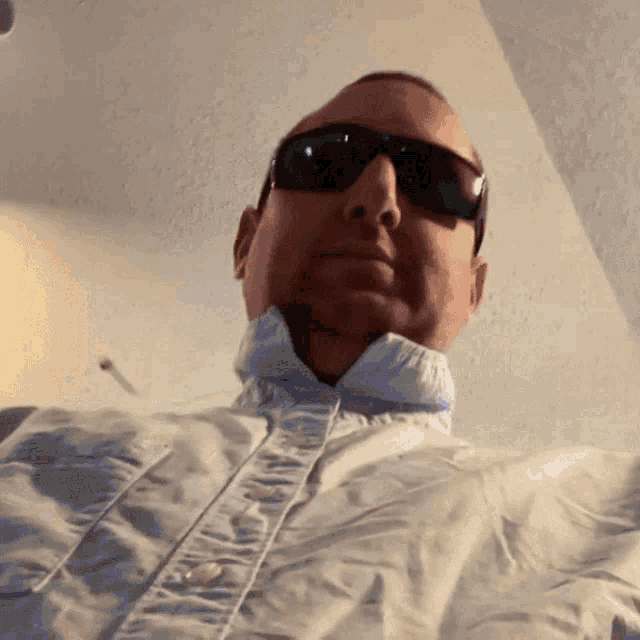a man wearing sunglasses and a white shirt looks down