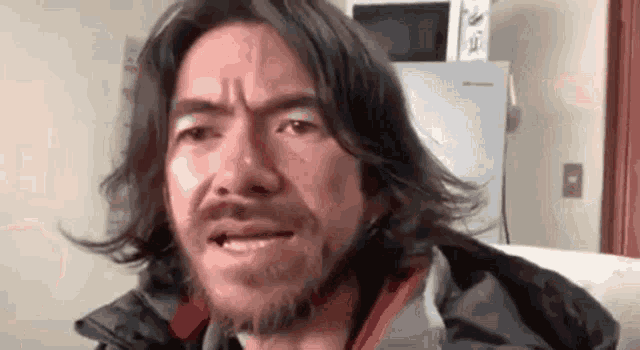 a man with long hair and a beard is making a face .