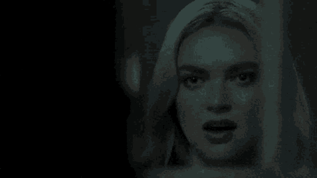 a close up of a woman 's face in a dark room looking out a window .