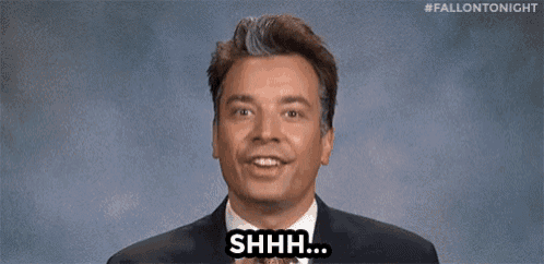 a man in a suit and tie is holding his finger to his mouth and saying shh .