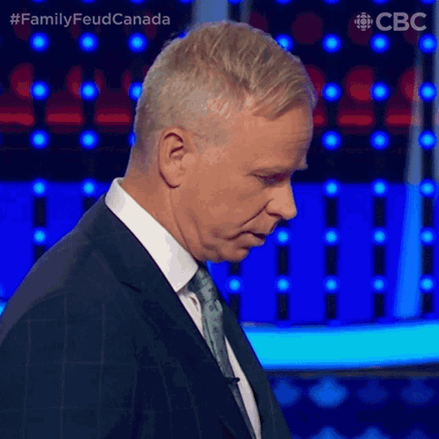 a man in a suit and tie is standing in front of a blue background with the words family feud canada on it