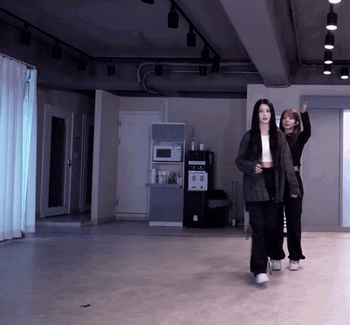 two women are walking in a room with a water dispenser on the wall