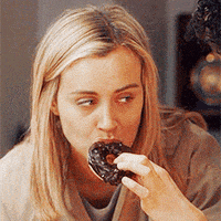 a woman is eating a chocolate donut from someone 's hand .
