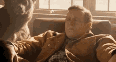 a man is sitting in a chair with a bear behind him