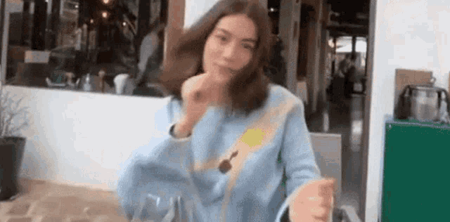 a woman in a blue sweater is sitting at a table with a spoon in her mouth .