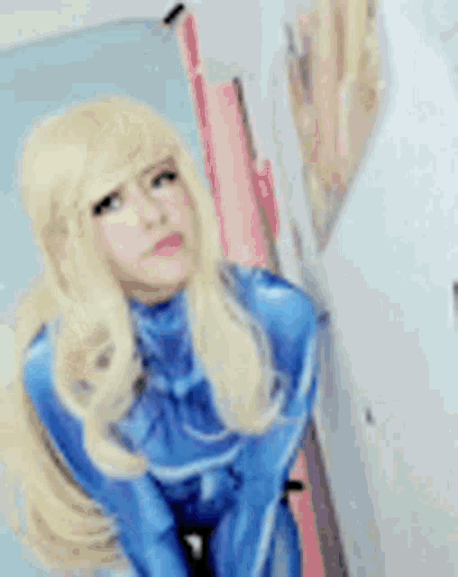 a woman in a blue costume with blonde hair is standing next to a wall .
