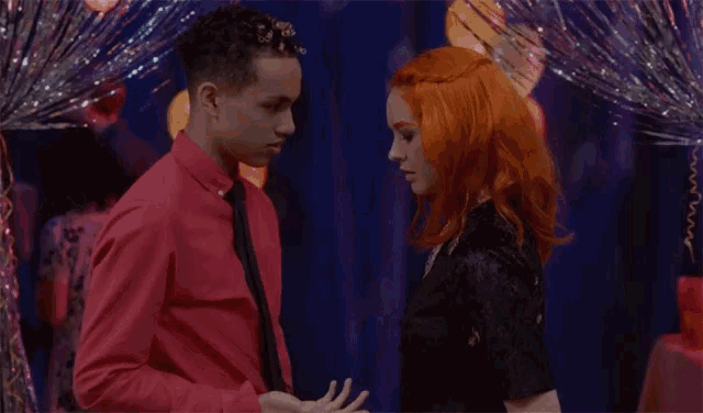 a man in a red shirt and tie is holding hands with a woman with red hair
